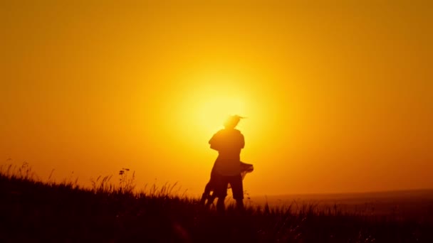 Loving couple - young man and beautiful girl dancing on summer meadow at sunset and have hugs and kiss, silhouette — Stock Video