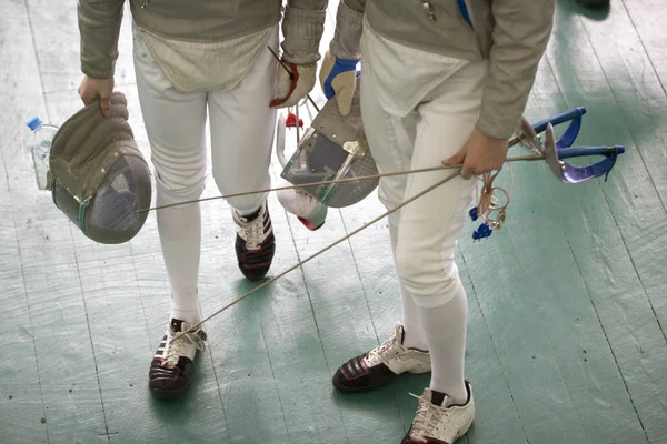 Ноги двух молодых фехтовальщиков, держащих мечи и защитную маску на соревнованиях по фехтованию — стоковое фото