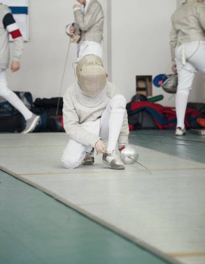 Fencer rapier ve koruyucu maske ile beyaz kostüm ayakkabı bağı bağlar