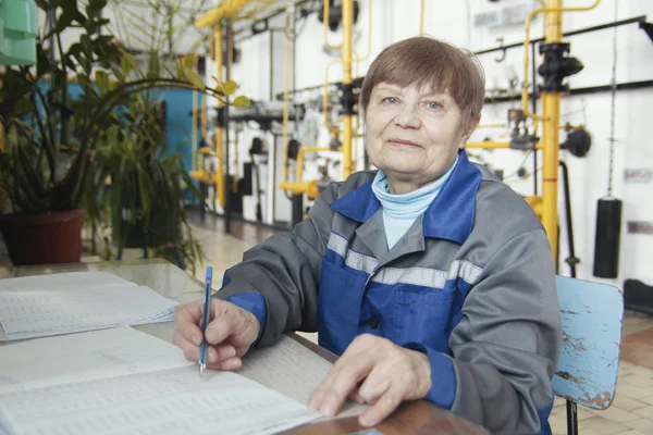 Mujer anciana sonriente en ropa de trabajo está escribiendo en el lugar de trabajo — Foto de Stock
