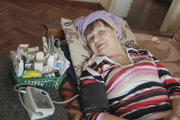 Mujer anciana enferma acostada en la cama con tabletas y dispositivo para medir la presión — Foto de Stock