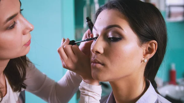 Artista visage professionale facendo make-up con eyeliner nero per bella donna — Foto Stock