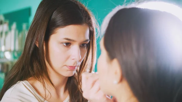 Estilista profesional hembra haciendo maquillaje para mujer joven delante del espejo en el salón de belleza — Foto de Stock