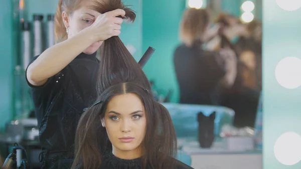 Makeup artist in beauty salon makes hair style for attractive girl, close up — Stock Photo, Image