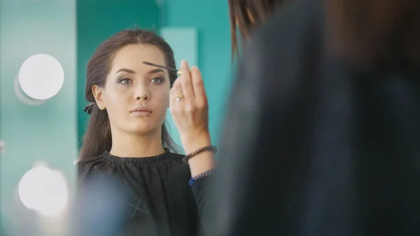 Makeup artist, hairdresser working with client in the beauty salon, shaping and coloring eyebrows