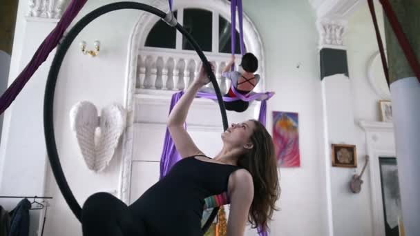 Two young women swinging on a hoop and making gymnastic elements on aerial silk — Stock Video