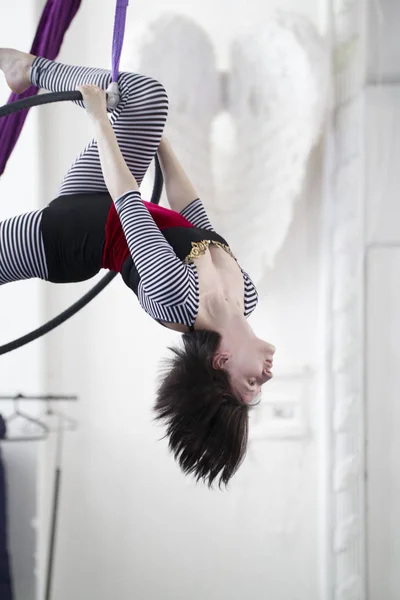 Flexible woman gymnast hangs upside down on the aerial hoop