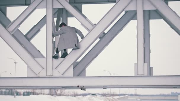 Młody człowiek wspinaczka pod mostem w pochmurny dzień — Wideo stockowe
