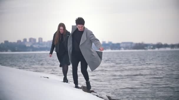 Feliz joven pareja corriendo a la orilla del río nevado — Vídeos de Stock