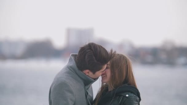 Счастливые молодой человек и женщина целуются на берегу реки — стоковое видео