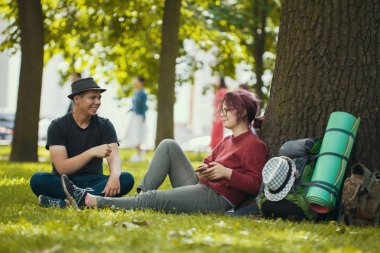 Çimenlerin üzerinde oturan genç mutlu yürüyüşçü görüşmeler