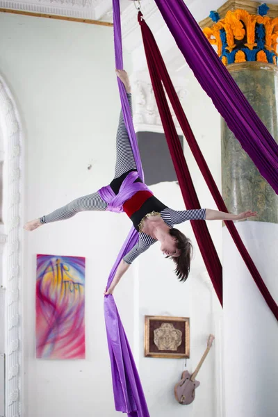 Back of young woman hangs upside down on the aerial silk