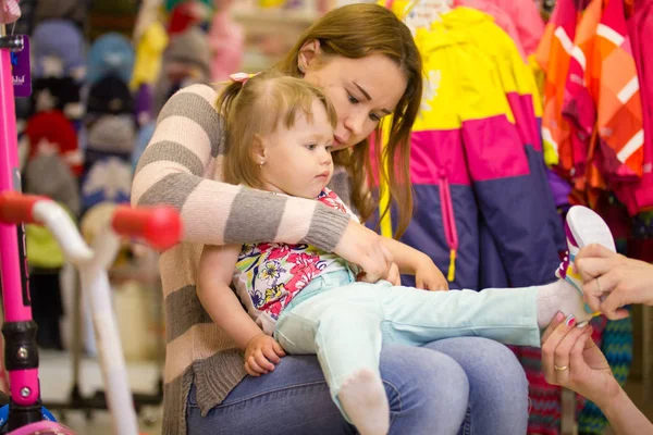 Mujer joven con hija pequeña eligiendo zapatos durante las compras — Foto de Stock