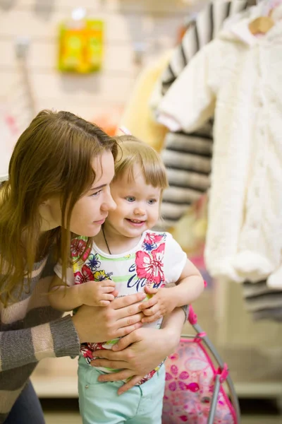 Mujer joven y su hija sonriendo en la tienda de ropa para niños — Foto de Stock