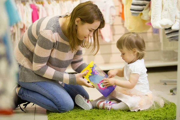 Joven madre con hija pequeña jugando con juguetes en la tienda de niños — Foto de Stock