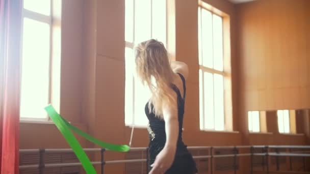 Mulher de cabelo loira jovem treina com uma fita verde - exercício de ginástica em estúdio com espelho — Vídeo de Stock