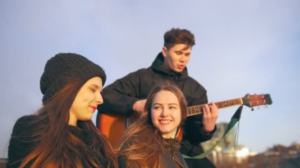 Vrolijke vrienden zingen met de gitaar bij de zonsondergang buitenshuis — Stockvideo