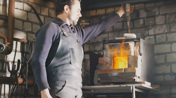 Il fabbro regola il fuoco nel forno con la ghisa — Foto Stock