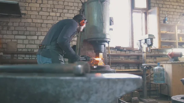 Molten metal is processed under pressure in the hands of a blacksmith, wide angle