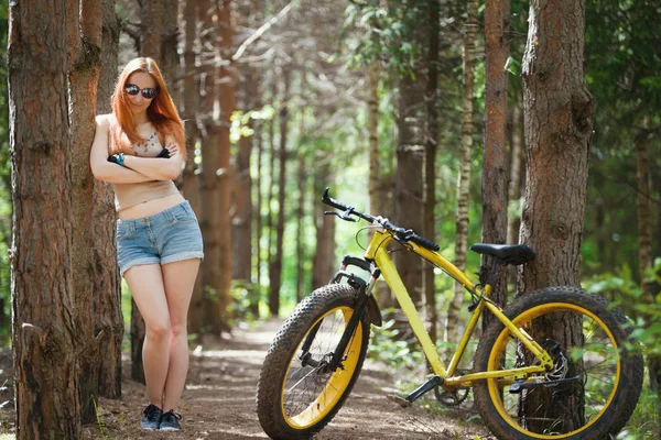 Привлекательная молодая женщина стоит рядом с деревом в лесу на велосипеде — стоковое фото