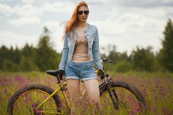 Привлекательная молодая женщина в спортивной одежде на цветочном поле с велосипедом — стоковое фото