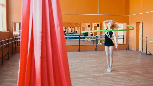 Rhythmic gymnastics - young woman training a gymnastics exercise with a green ribbon