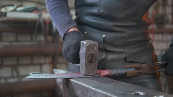 Uomo muscoloso fabbro con martello in fucina creando coltello in acciaio — Foto Stock