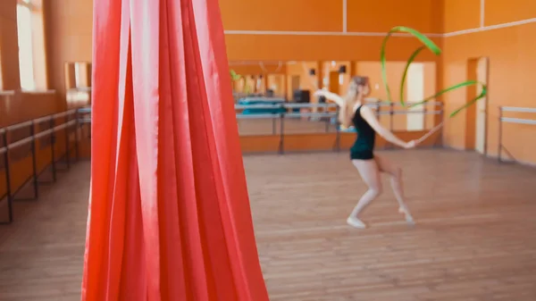 Красный шелк перед молодой женщиной, тренирующей гимнастические упражнения с лентой - рассеянный — стоковое фото