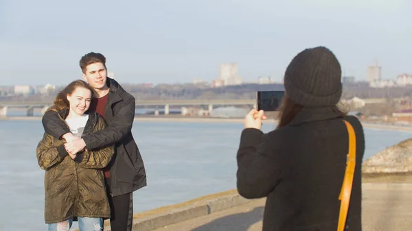 Girl takes a photo for her friends couple at the walk on the waterfront — Stock Photo, Image