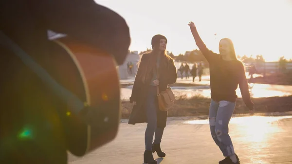 Чоловік грає на гітарі перед молодими танцюючими дівчатами на заході сонця — стокове фото