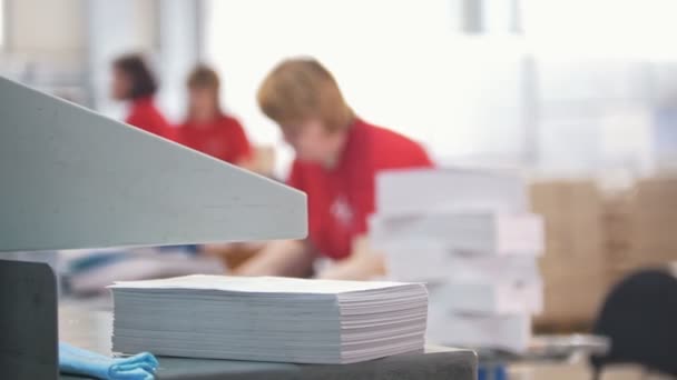 Бумажная стопка перед женщинами, работающими в типографии - децеленаправленно — стоковое видео