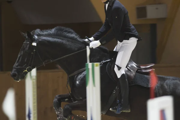 Young rider on black horse galloping at show jumping competition — Stock Photo, Image