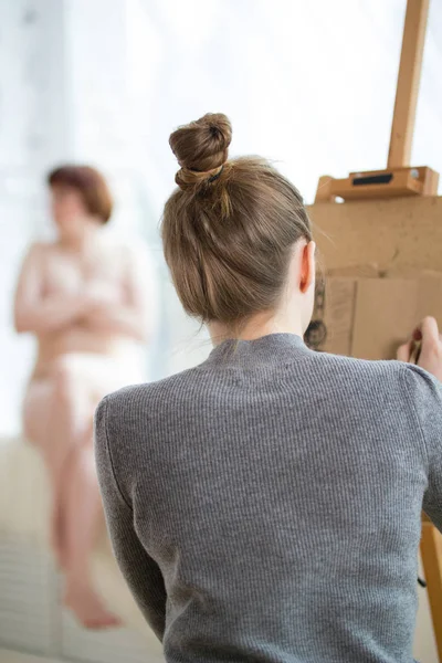 Назад жіночого художника малює на мольберті оголена жінка — стокове фото