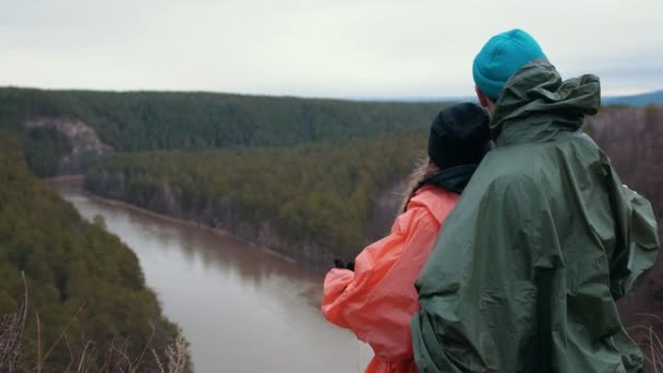 Молода біла пара стоїть на схилі пагорбів над гірською річкою, насолоджуючись прекрасною природою — стокове відео