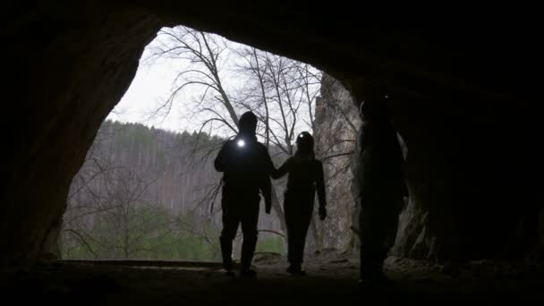 Young hikers silhouette in helmet enters from the forest to the dark cave with flashlight — Stock Video