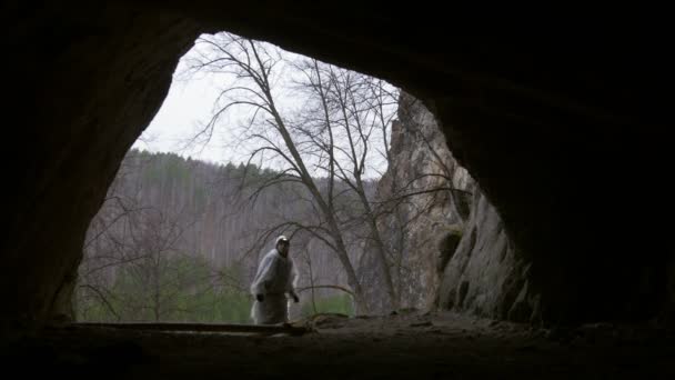 Giovane escursionista in casco entra nella grotta buia con torcia elettrica e foresta profonda sullo sfondo — Video Stock