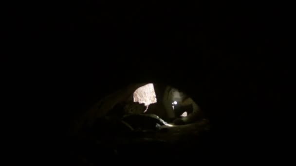 Young explorer in helmet scrambles on all fours into the dark cave — Stock Video