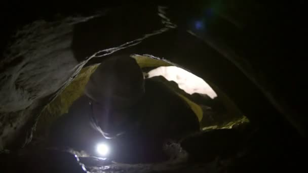 Jeune homme rampant à travers un trou étroit dans la grotte avec une lampe de poche dans sa main 