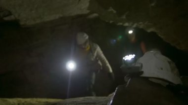 Kask speleologists önünde el feneri ile karanlık dar mağaraya araştırıyor