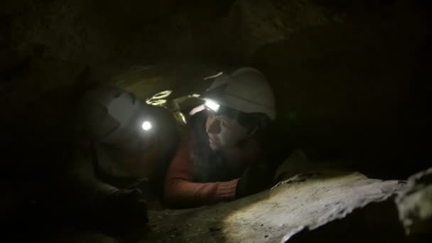 Dva mladí turisté průzkumníci strčil do úzkého otvoru v temné jeskyni — Stock video