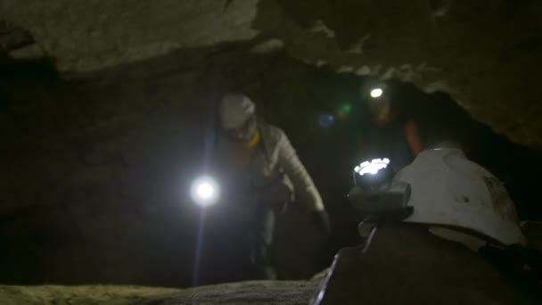 Helmet with flashlight in front of speleologists explores into the dark narrow cave — Stock Video