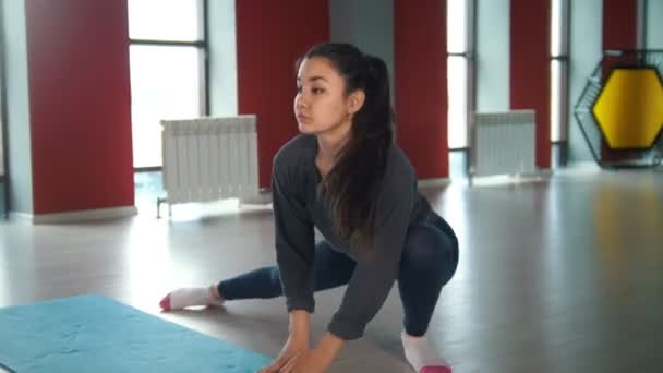 Jonge slanke vrouw haar benen in rode fitnessruimte uitrekken — Stockvideo