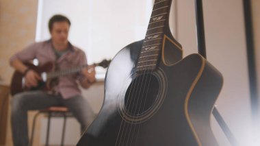 Young attractive musician composes music on the guitar and plays, other musical instrument in the foreground, blurred clipart