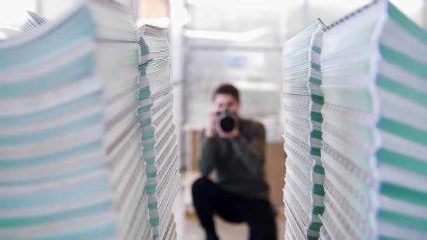 Joven fotógrafo profesional disparando delante de pilas de papel en la tipografía — Vídeos de Stock