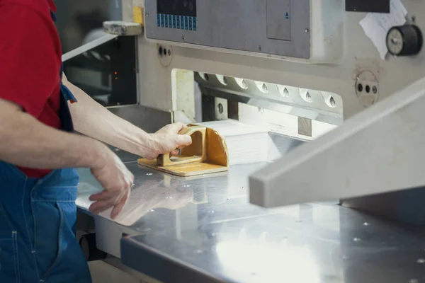 Руки робітника в типографії кладуть папір на машину для різання гільйотини — стокове фото