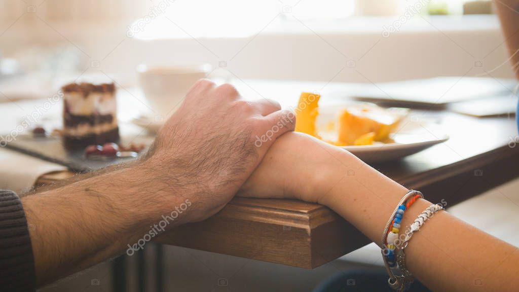 Holding hands of young couple in the cafe enjoying the desserts