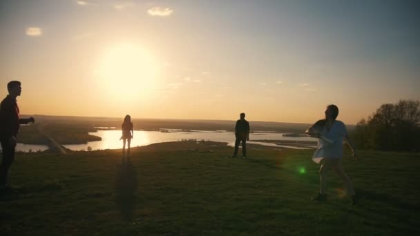 Vários jovens jogando frisbee na colina ao pôr do sol — Vídeo de Stock