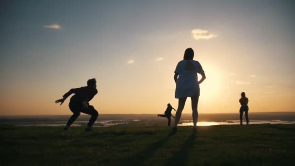 Jovens amigos felizes jogando frisbee na colina ao pôr do sol — Vídeo de Stock