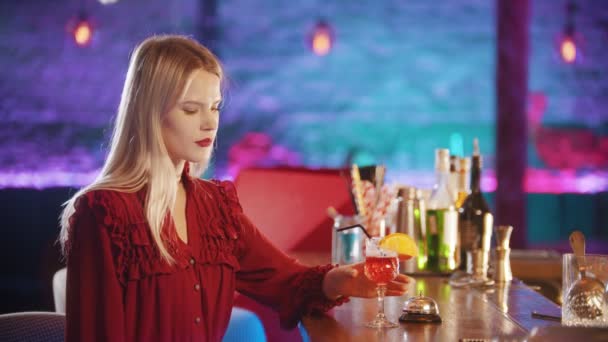 Superbe jeune femme blonde avec du rouge à lèvres rouge assis près du stand de barman boire une boisson rouge de la paille — Video