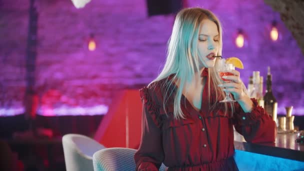 Прекрасная молодая женщина, сидящая у бармена, пьет коктейль - поворачивается и поворачивается назад — стоковое видео
